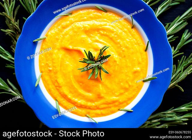 pumpkin soup with rosemary branches on a black background with a blue napkin