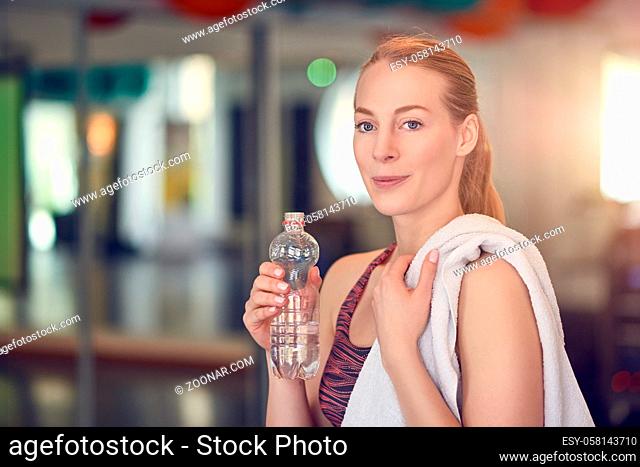 Young woman athlete drinking bottled water for hydration after working out in a gym in a health and fitness concept