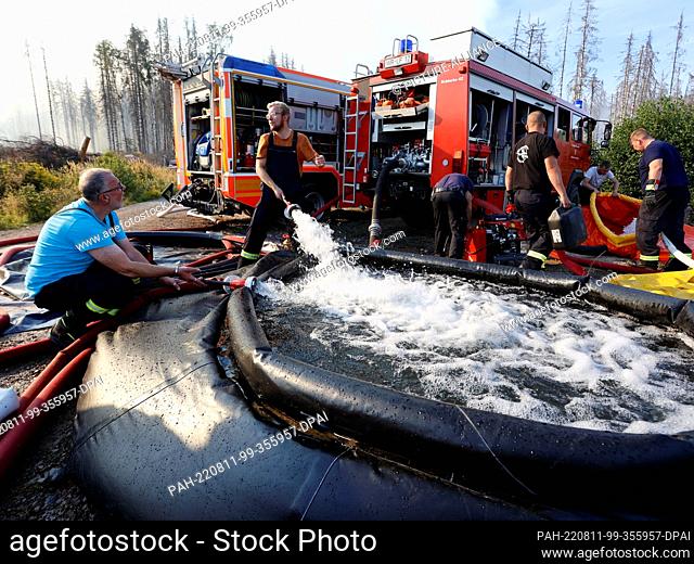 11 August 2022, Saxony-Anhalt, Schierke: Firefighters fill a collapsible water tank with water as they fight a major forest fire in Schierke
