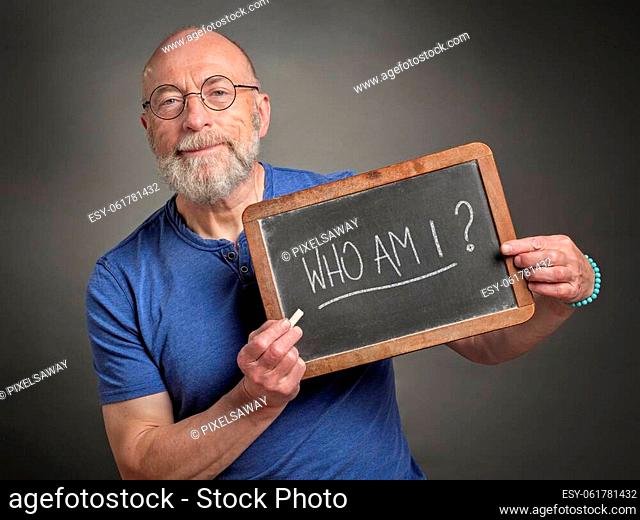 Who am I? Senior man is sharing inspirational question handwritten on a blackboard. Philosophy, identity and personal development concept