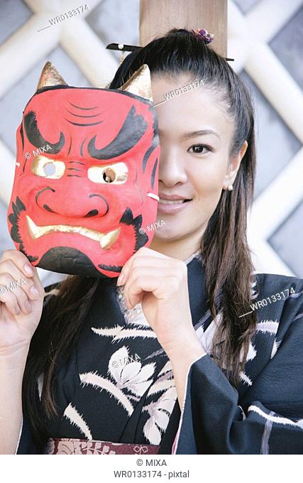 Young woman in kimono holding mask up to face