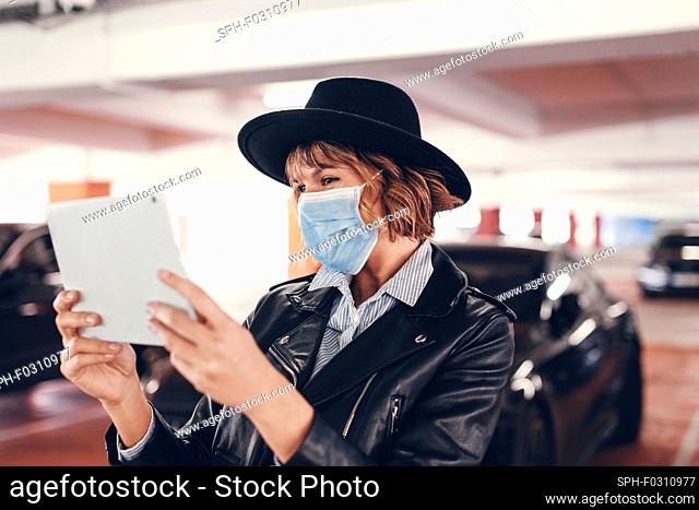 Young urban woman in mask and hat using tablet