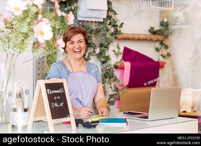 Mature female flower shop owner laughing while standing at checkout