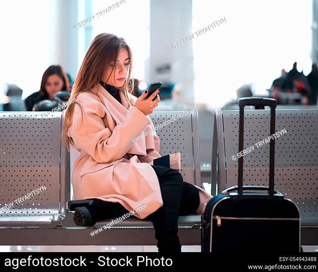 Airport business woman waiting in terminal. Air travel concept with casual businesswoman sitting with suitcase. Mixed race female professions