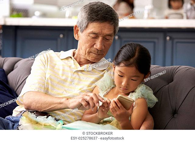 Grandfather And Granddaughter Using Mobile Phone At Home