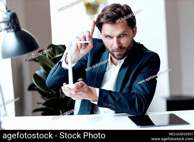 Mature businessman pointing while holding wind turbine model in office