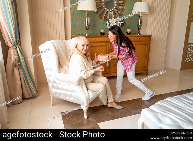 Excited Young Daughter Surprises Her Senior Mother With A Birthday Present. General Shot Of Two Happy Women When Of Them Gives A Present To The Other One