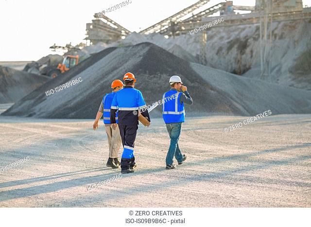 Three quarry workers, walking across quarry, rear view