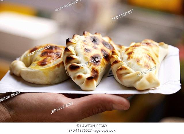 A hand holding a paper plate of empanadas at a market