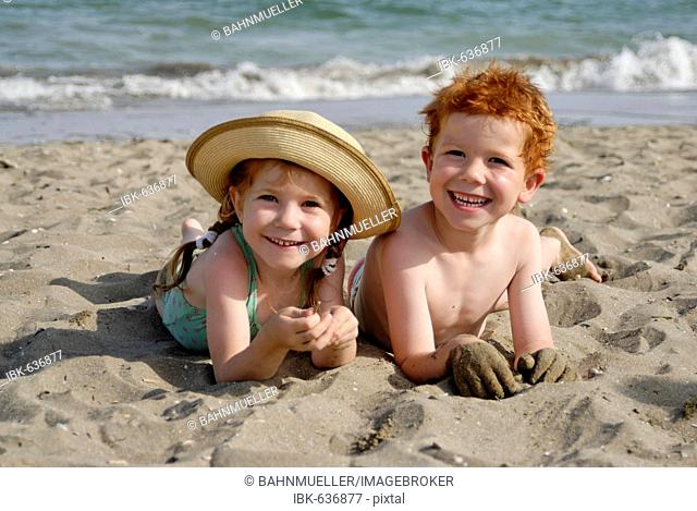 Two children are lying on a sandy beach at the sea