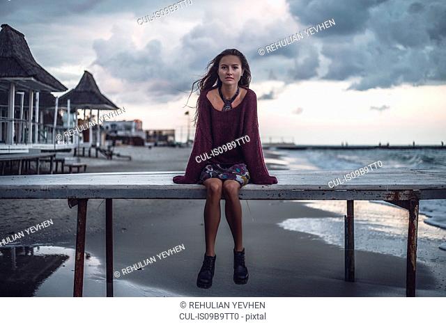 Portrait of young woman sitting on pier at dusk, Odessa Oblast, Ukraine