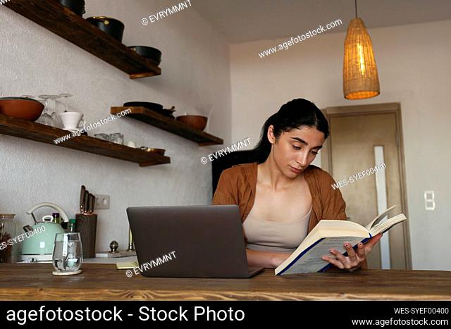 Woman studying with book and laptop on table at home