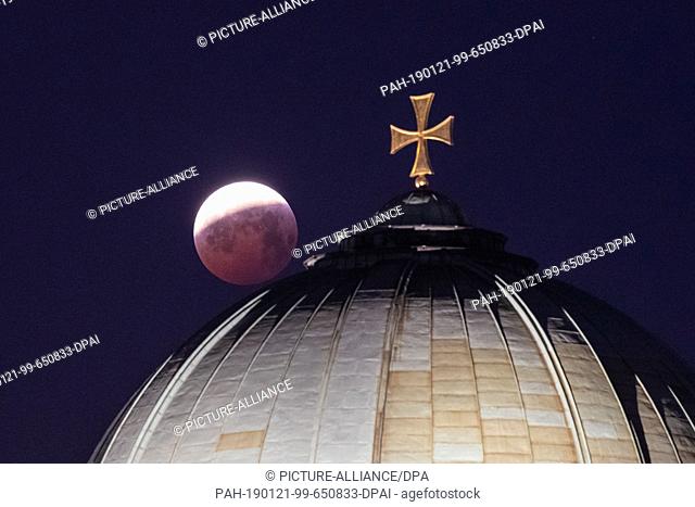 21 January 2019, Bavaria, Nürnberg: As a red, so-called ""blood moon"" the full moon stands over the dome of the church St