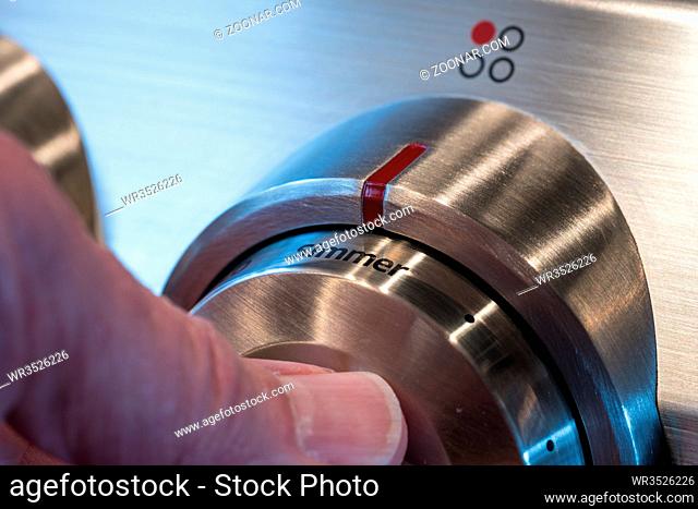 Hand on stainless steel control knob on induction cooktop or hob set to simmer