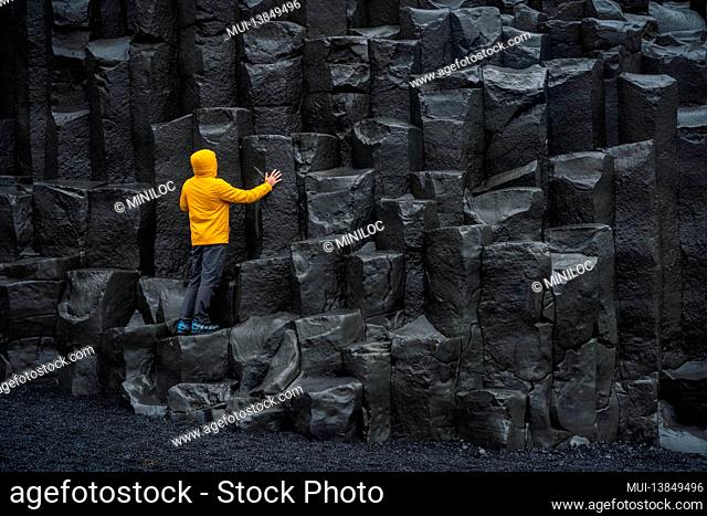 Adult man in yellow jacket standing on basalt columns on Reynisfjara Black Sand Beach in Iceland