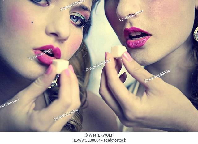 The faces of two young women wearing pink lipstick holding sugar cubes