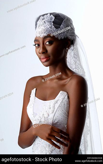 Beautiful black skin young woman in white gown and lace veil. Beauty shot on light background. Copy space