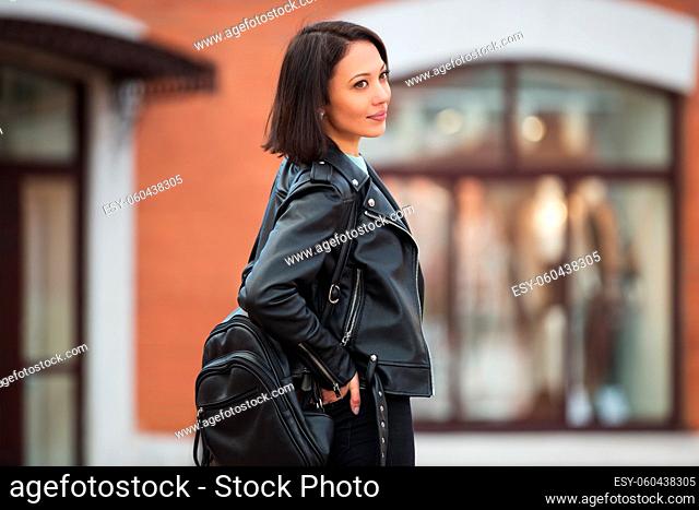 Young fashion woman with backpack walking in city street Stylish female model in black leather jacket outdoor