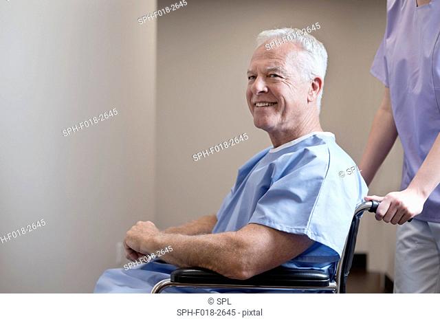Senior man in hospital gown in wheelchair, smiling