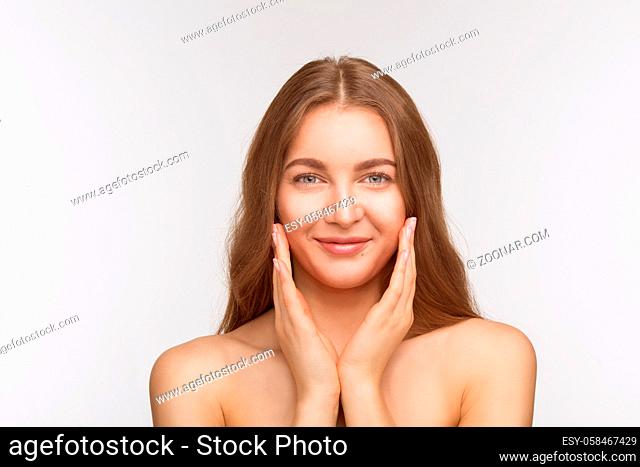 Portrait of happy smiling beautiful shirtless lady looking at camera and touching her fce skin over white background in studio