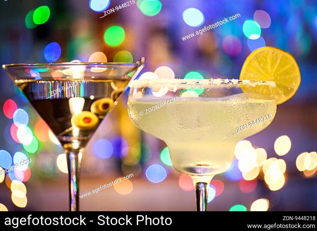 Glasses of margarita and martini cocktails on bar lights background