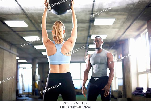 Trainer watching female client lift medicine ball in gym
