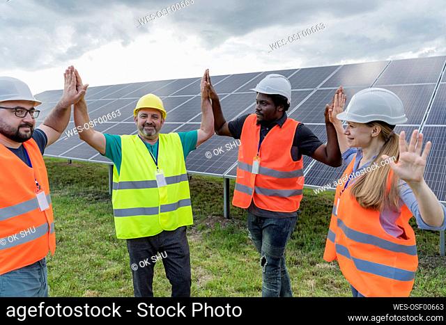 Smiling engineers high-fiving and standing in front of solar panels at field