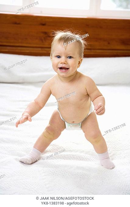 Happy Emotional Naked Ten Month Old Baby Girl Standing on Bed