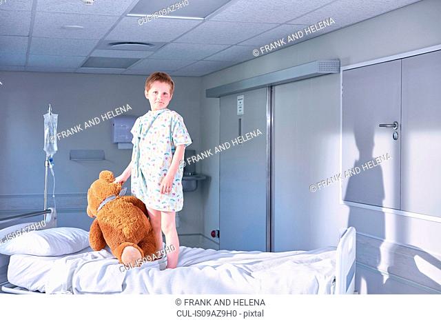 Portrait of boy patient on bed holding teddy bear on hospital children's ward
