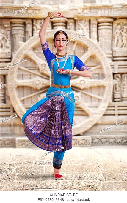 Full length of female Bharat Natyam dancer performing against carved wall