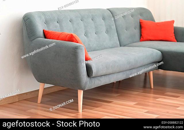 Modern gray couch with red pillows on wooden tiled floor - office furniture