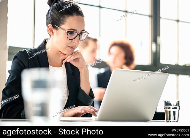 Concentrated business woman reading important information on laptop while sitting at desk in the office