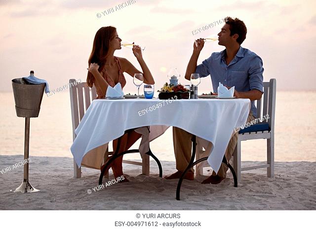 Romantic young couple drinking champagne while having dinner on the beach