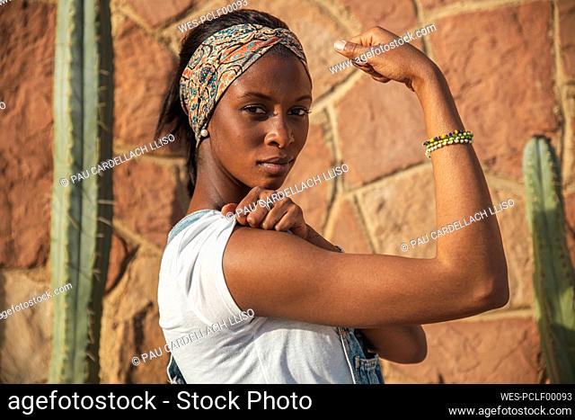 Confident woman flexing muscle in front of wall with cactus plant