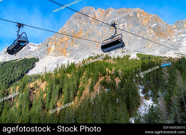 Alpine scenery with the rocky peaks of the Alps mountains and ski lifts rolling on a cableway over the snowy fir forests, in Ehrwald, Austria