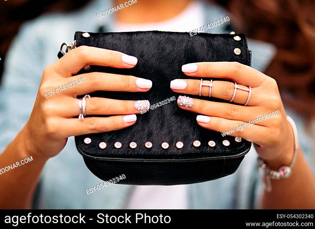 Close-up of unrecognizable woman with beautiful trendy manicure wearing wedding set and jewelry holding small black fancy handbag