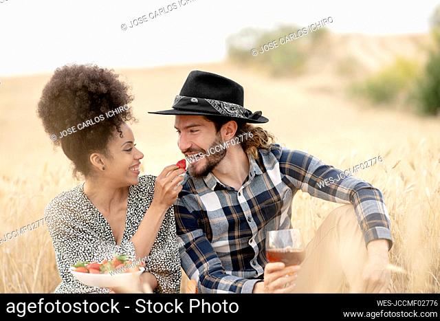 Woman feeding strawberry to man while sitting on field during picnic