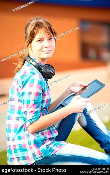 Preparing to exams outdoors. Beautiful young female student writing or reading something from note pad. Woman sitting on bench in city park