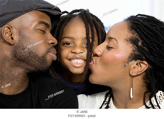 A mother and father kissing their son on the cheek