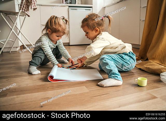 Two kids sitting on the floor and taking colored pencils out of the cardboard box