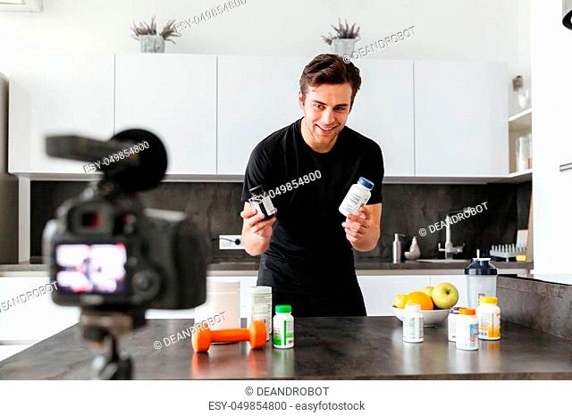Excited young man filming his video blog episode about healthy food additives while standing at the kitchen table
