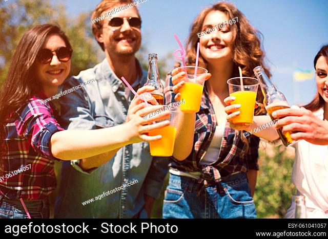 Cheerful group of friends toasting their drinks. Happy young people spending time outdoors on sunny day cheering their orange juices