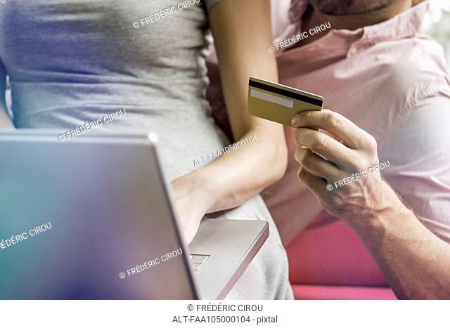 Couple using laptop computer and credit card to shop online, cropped