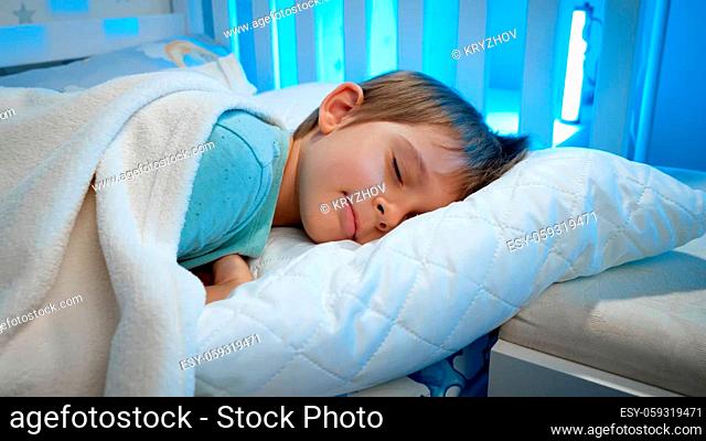 Portrait of cute toddler boy lying in bed and sleeping at night. Calm beautiful child in bed