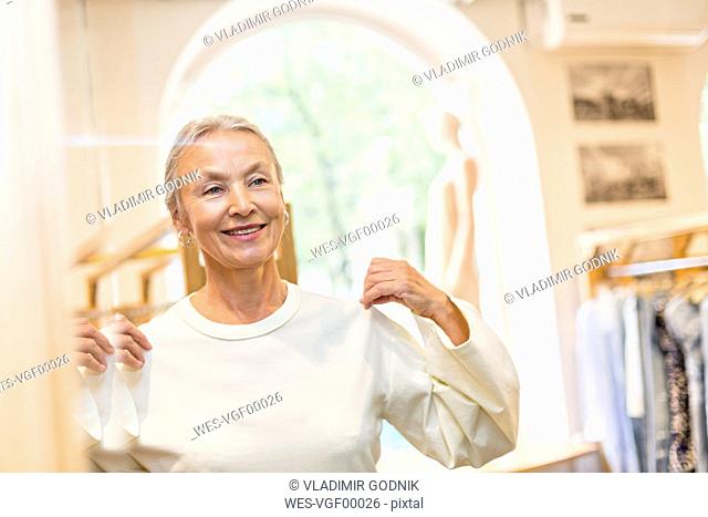 Smiling senior woman trying on pullover in a boutique