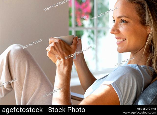 Smiling woman holding coffee mug at home