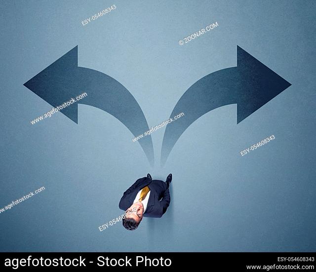 Young smart businessman standing in front of two arrows potinting to different ways contemplating a decision