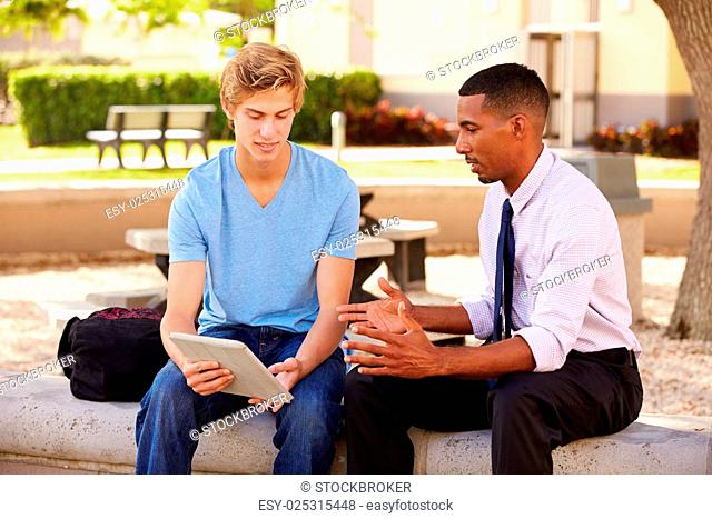 Teacher Sitting Outdoors Helping Male Student With Work