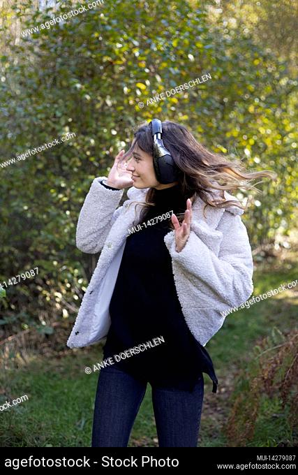 Young woman with headphones dancing to music in forest