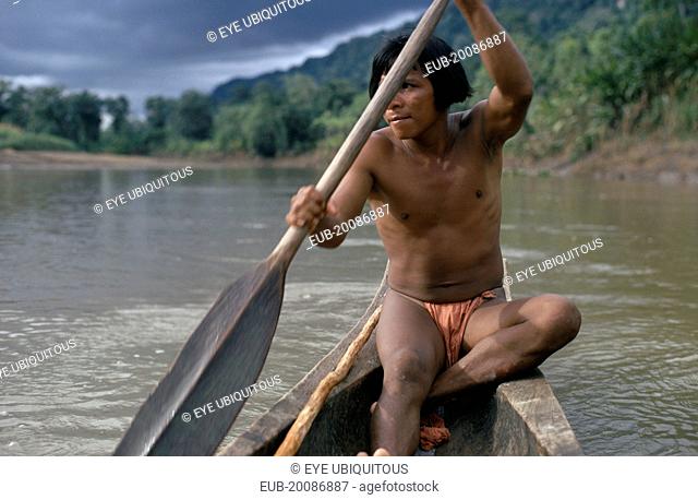 Embera man using single oar to steer wooden dug out canoe along rio Baudo.Pacific coastal region boat piragua tribe